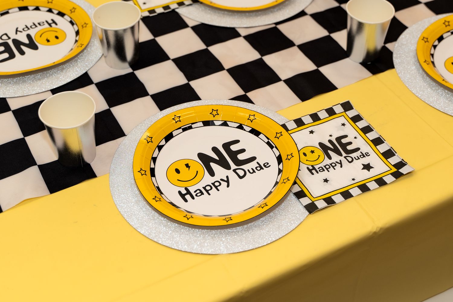 Yellow and black checkered party plates with smiley face design on table setting.