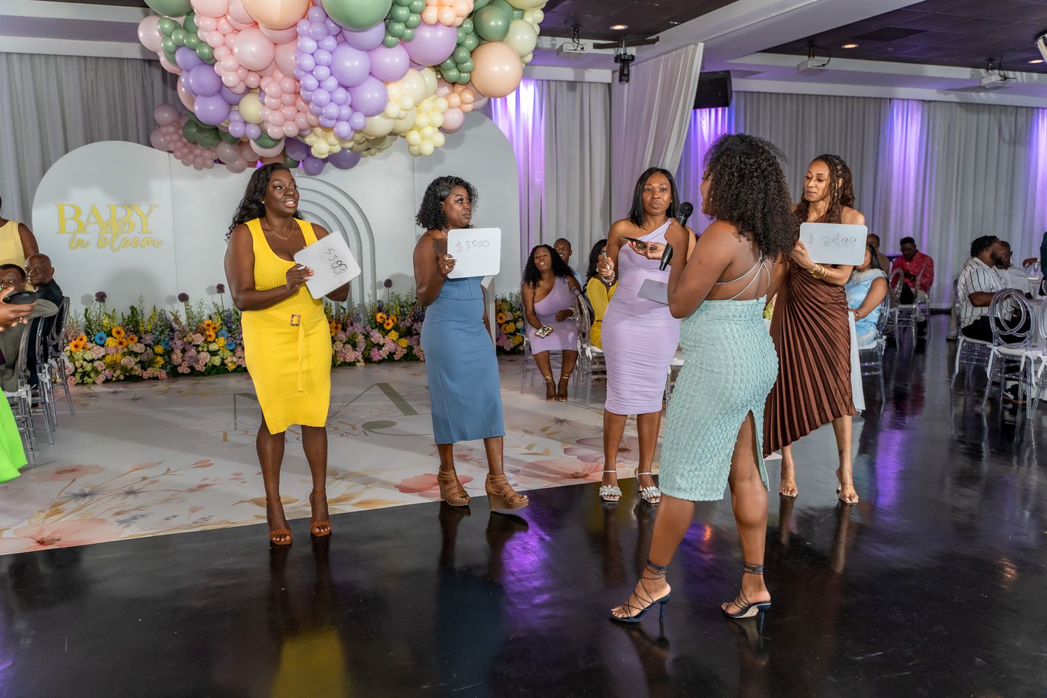 A group of guests in colorful dresses socializing on a dark floor at an event venue.