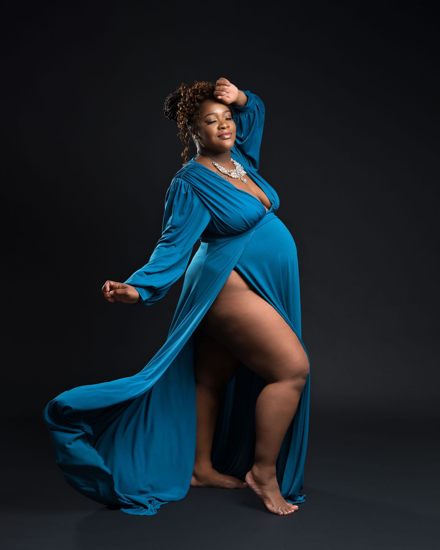 A dynamic maternity portrait shows an expectant mother in a flowing blue dress against dark backdrop.