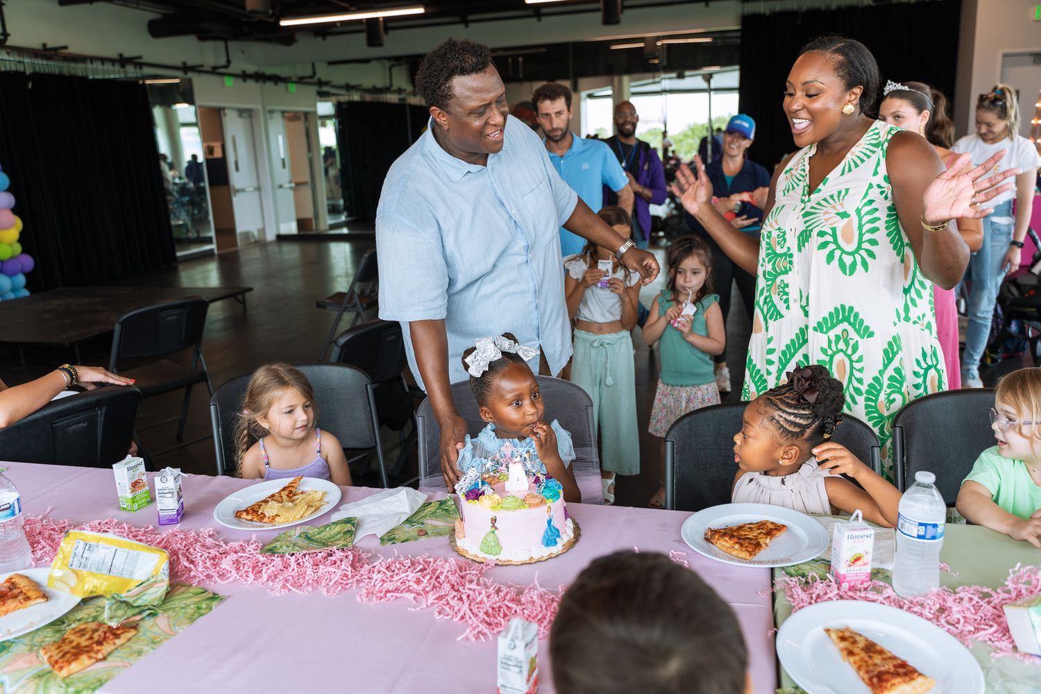 A birthday celebration with a pink-themed table setting and cake surrounded by guests enjoying the festivities.