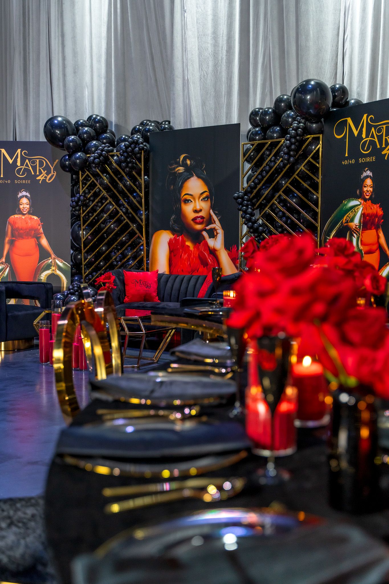Luxury event decor featuring posters, red roses, and black and gold table settings.