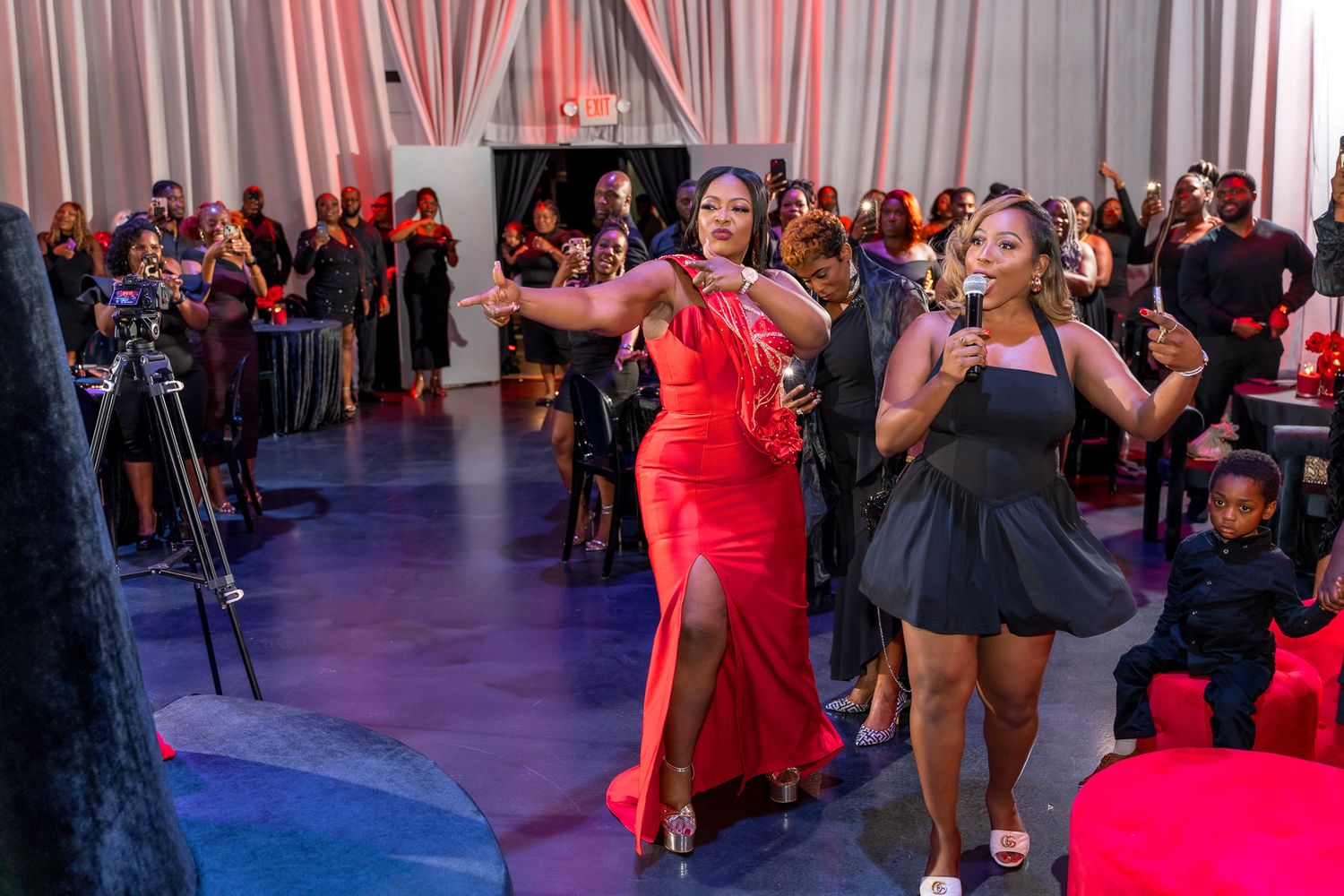 People dancing and celebrating at an indoor party with dramatic lighting and white curtain backdrop.