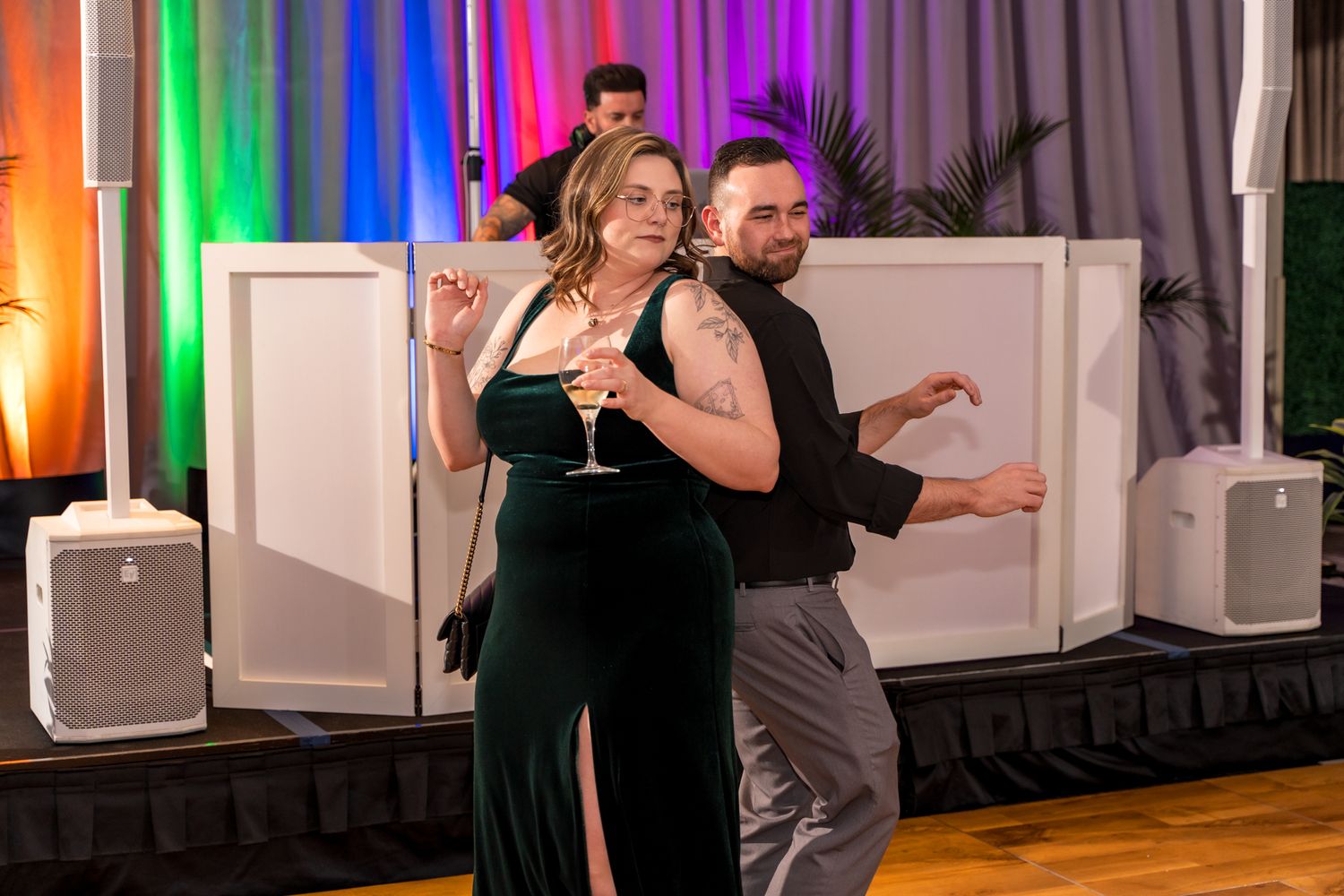 Dancers performing on a wooden dance floor with rainbow-colored lighting and speaker setup.