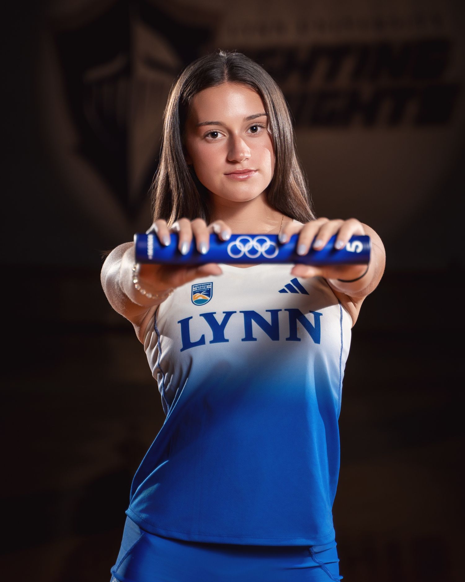 Athlete holding a relay baton while wearing a white and blue gradient uniform with Lynn branding.