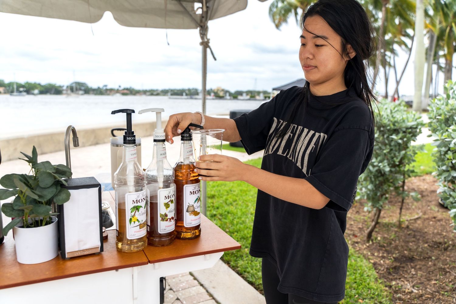 A barista prepares drinks at an outdoor coffee station by the waterfront.