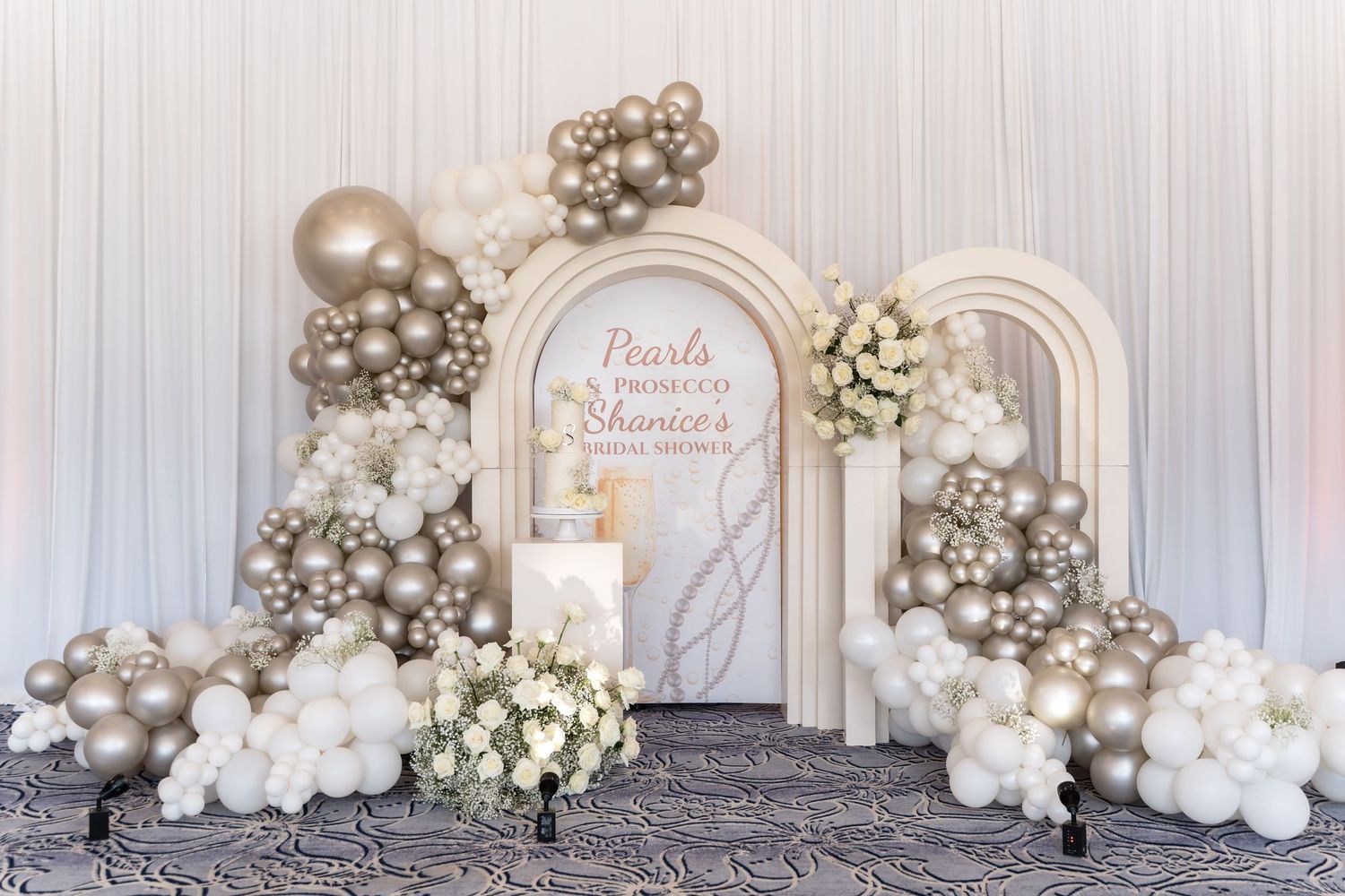 Luxurious wedding backdrop with white and silver balloons, roses, and elegant drapery for an ethereal celebration setup.