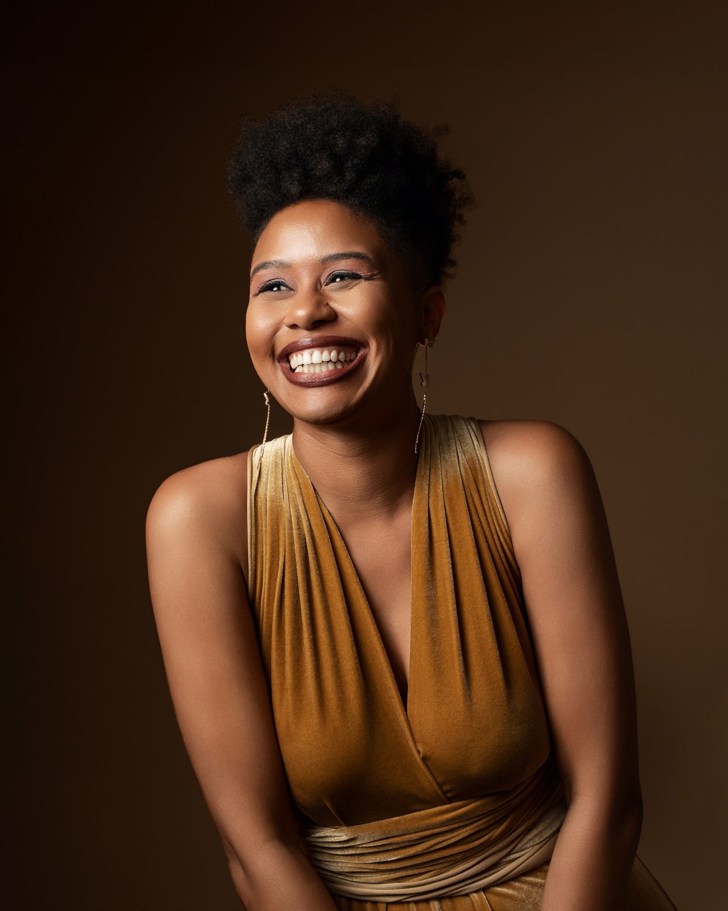 Woman in gold halter dress smiles brightly in studio portrait.