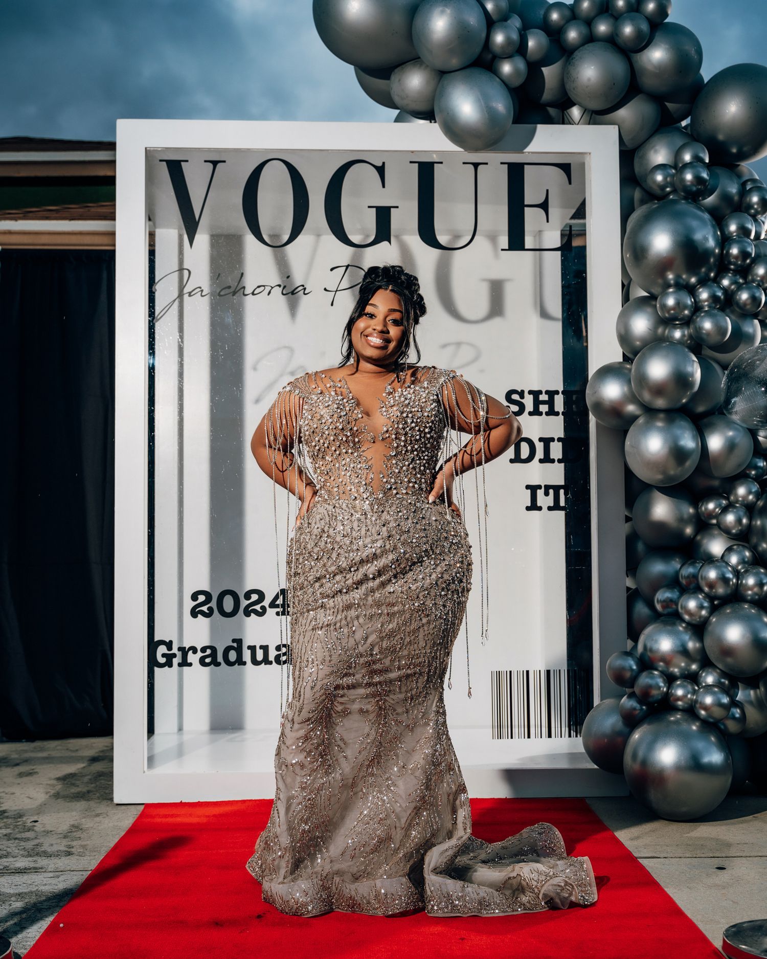 Glamorous graduation photo shoot with silver balloons and Vogue-style backdrop on red carpet.