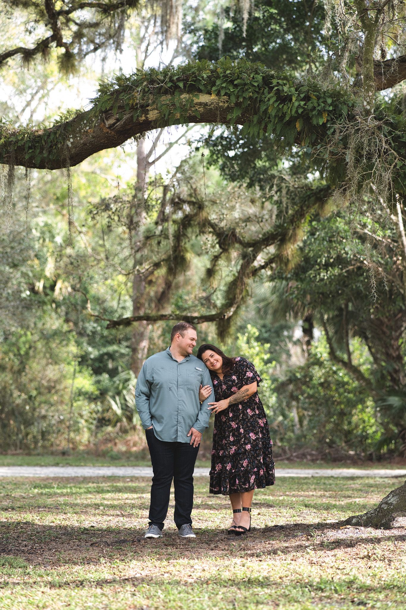 Couple standing under moss-draped oak tree in a natural setting.