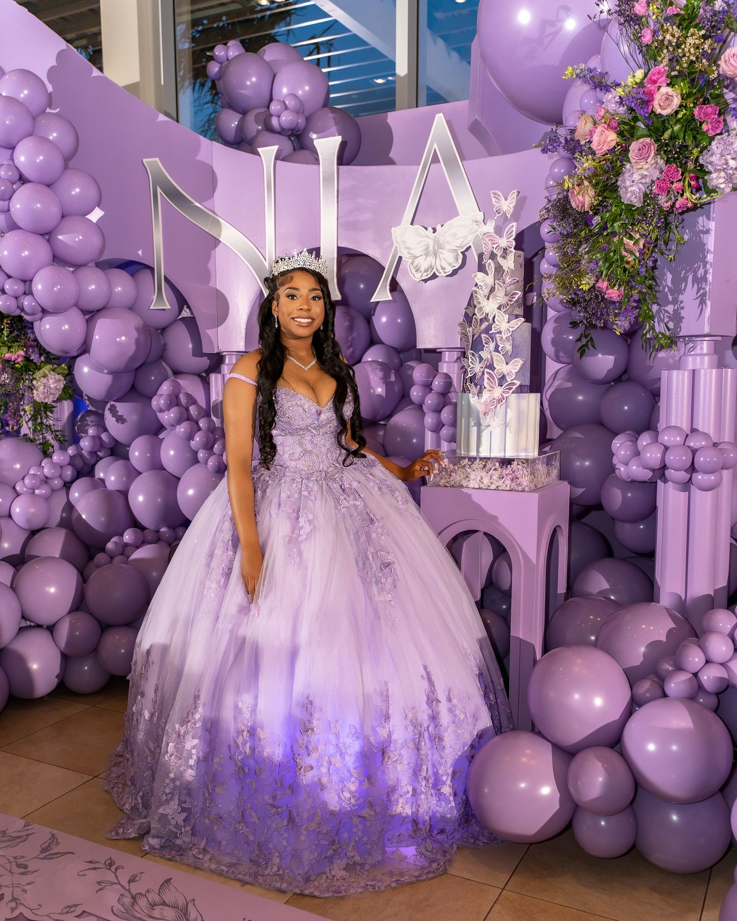 A lavender-themed celebration setup with balloon arches, floral decorations and a princess-style backdrop.