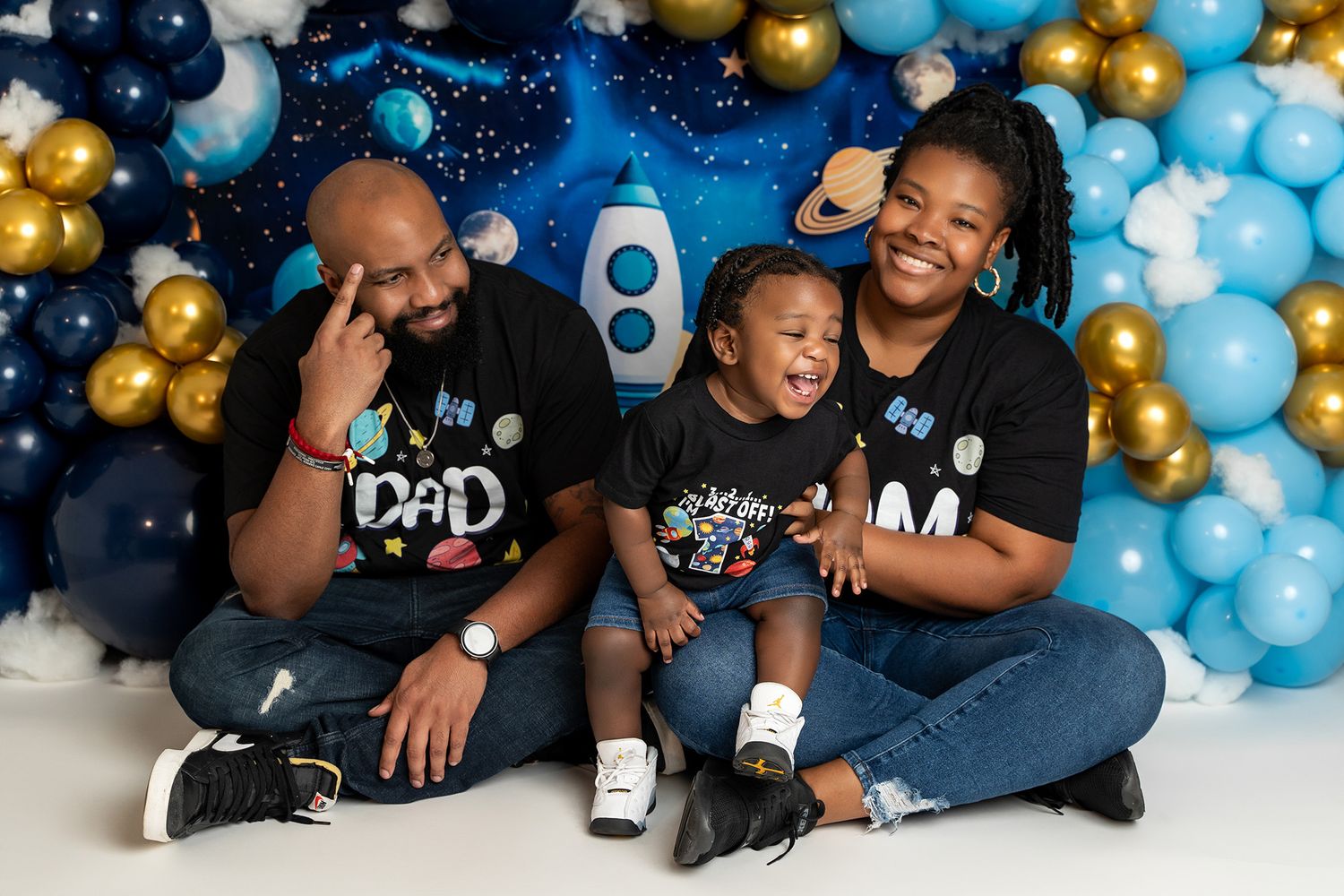 Happy family wearing matching t-shirts posing against festive balloon backdrop.