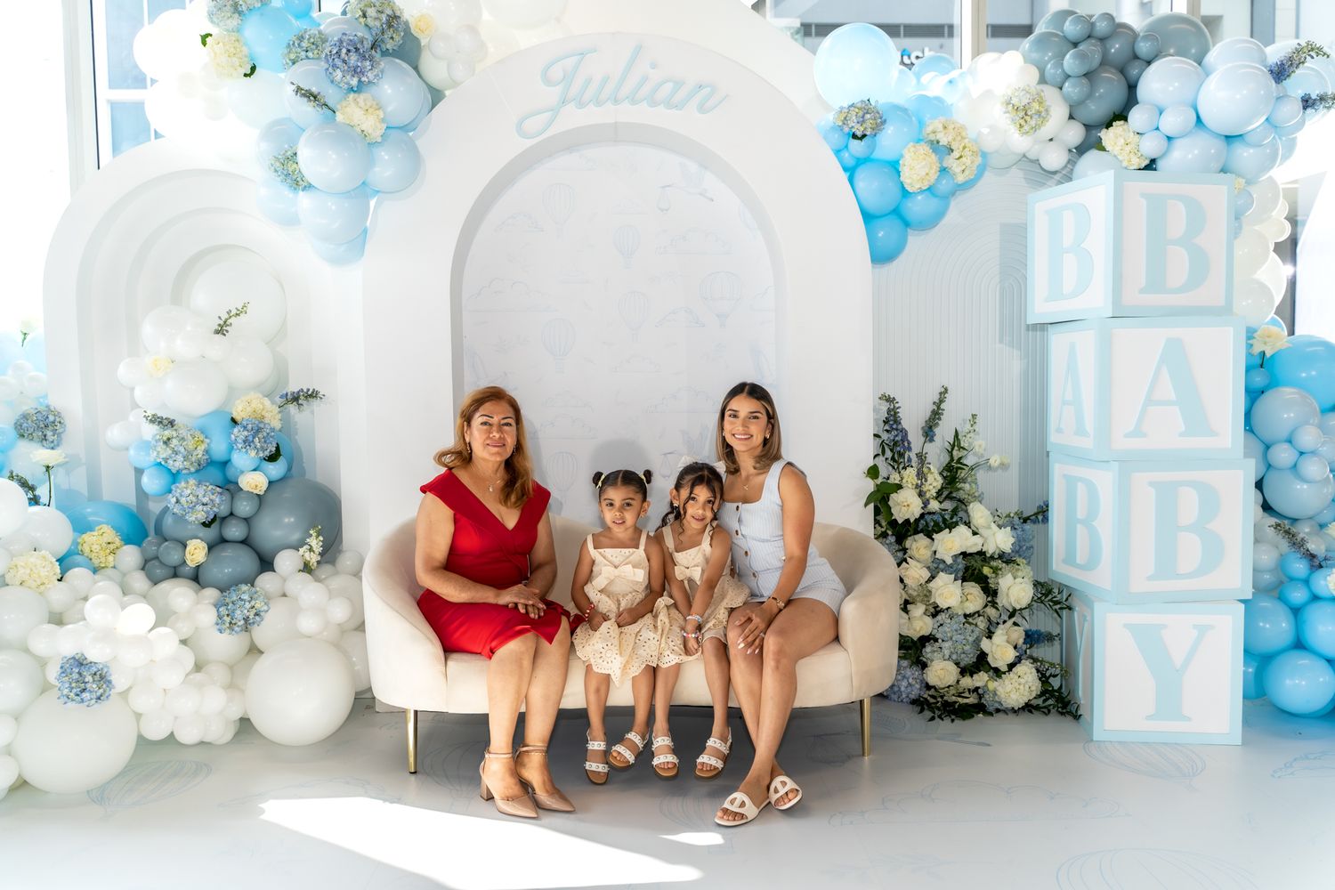 Baby shower backdrop with blue and white balloon arch and decorative letters.