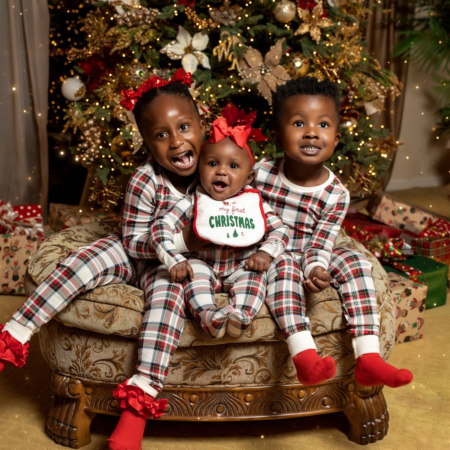 Three people in matching plaid Christmas pajamas pose in front of a decorated tree.