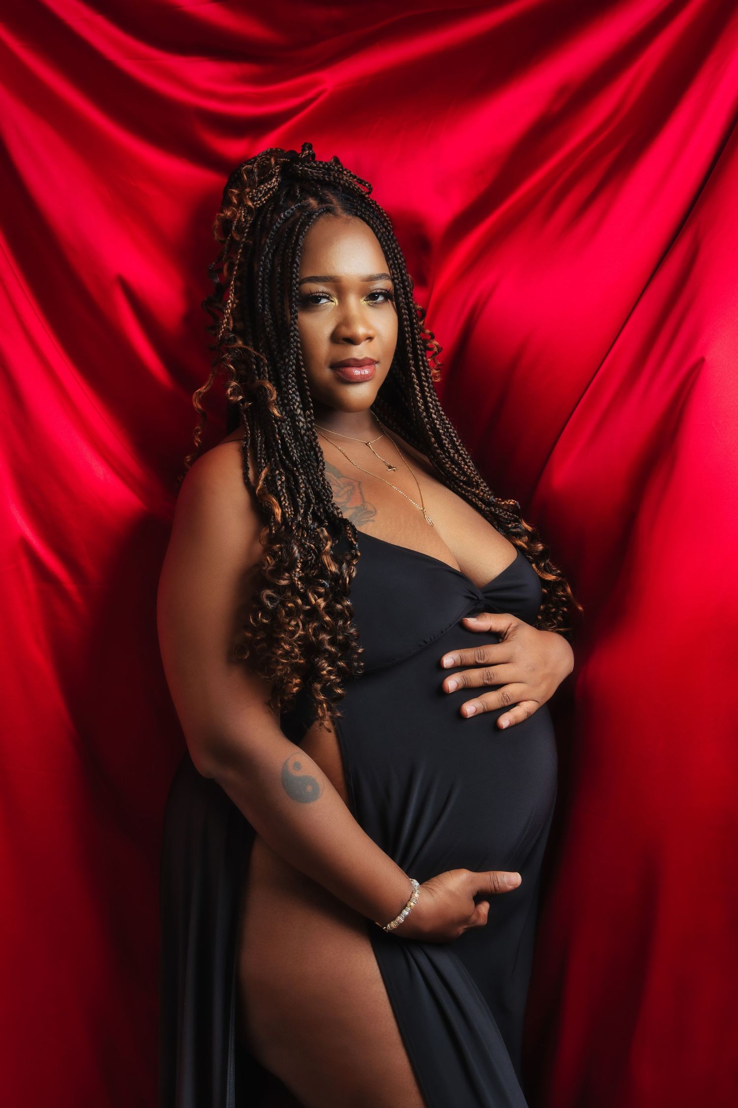 A glamorous maternity portrait against red satin features an expectant mother in a flowing black dress.