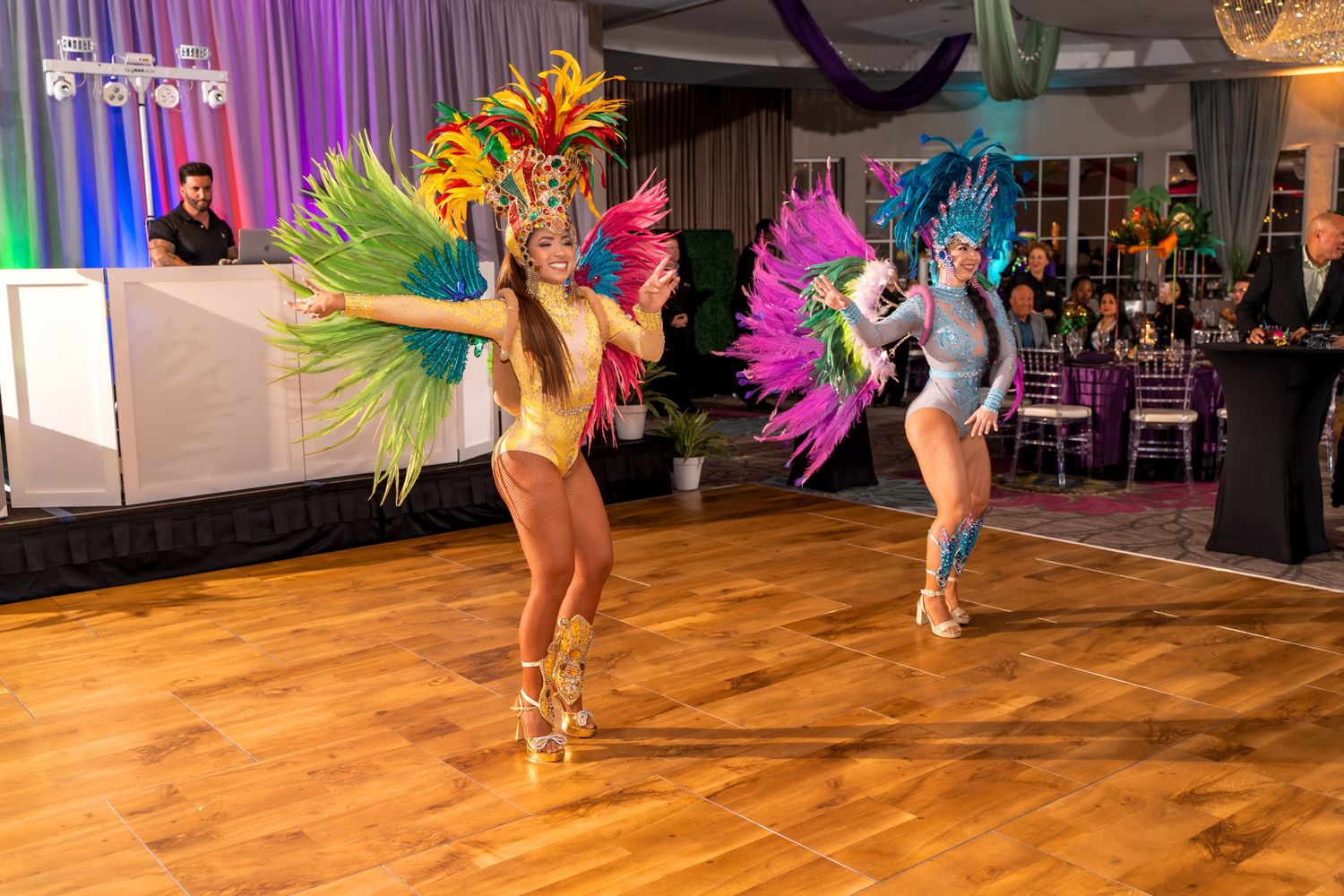 Dancers in vibrant carnival costumes performing on a wooden dance floor with colorful lighting.
