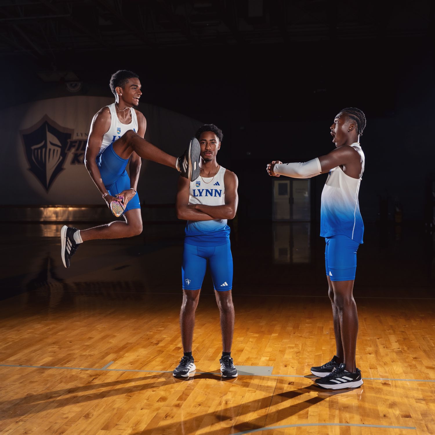 Athletes in blue and white uniforms demonstrating dynamic poses in a dark gymnasium.