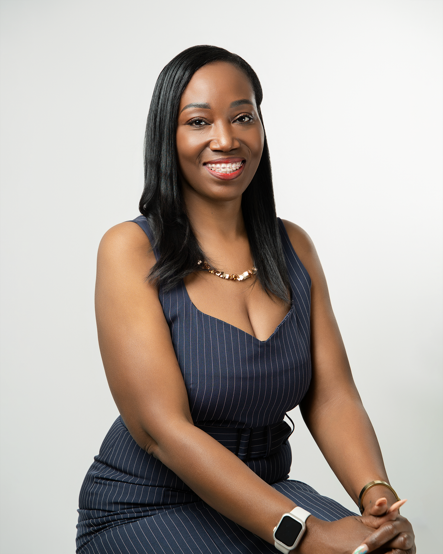 Professional headshot of someone in a navy pinstripe dress wearing a necklace against a light backdrop.