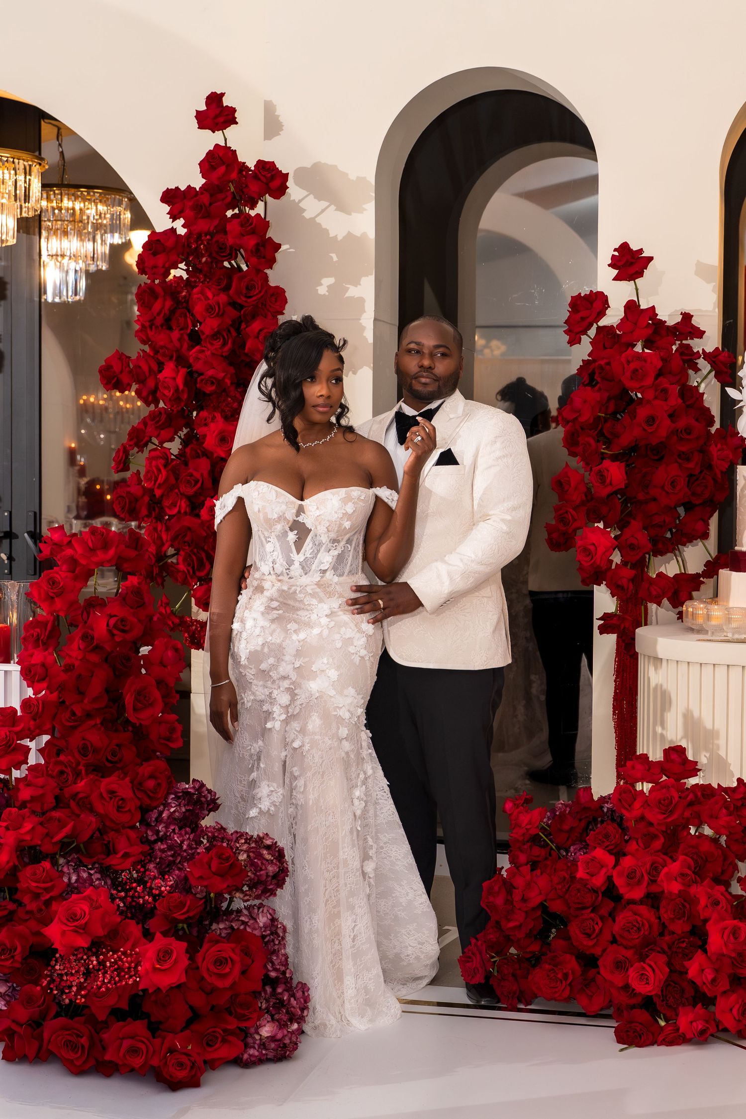 Wedding celebration space adorned with dramatic red rose floral installations and arched doorways.