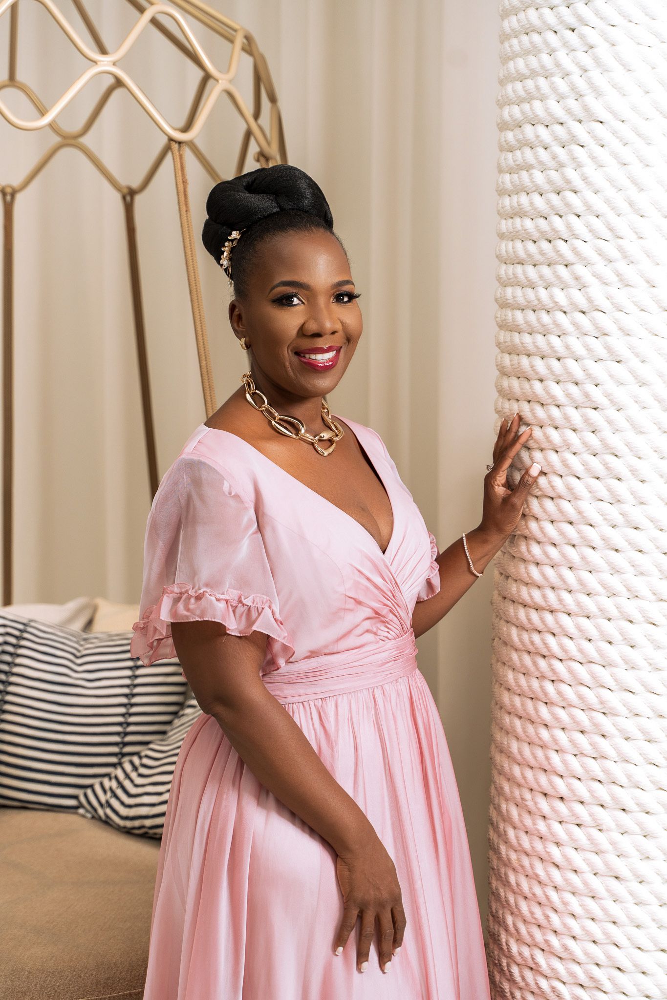Woman in pink vintage-style dress poses elegantly against textured wall.