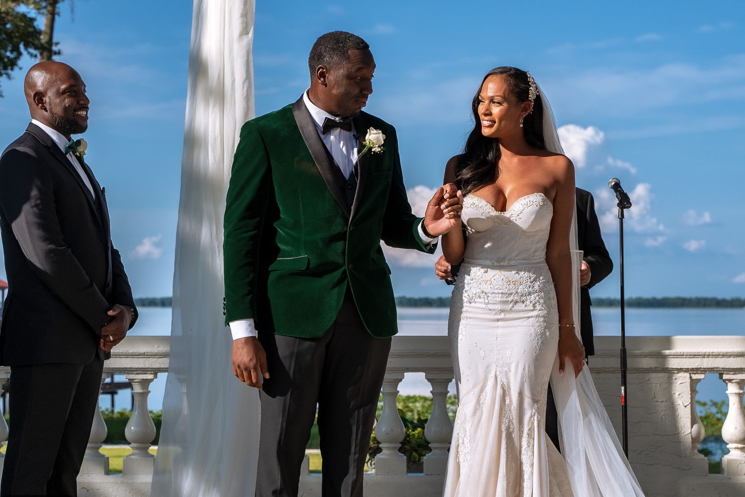 A couple celebrates during their wedding ceremony at an elegant waterfront venue with white columns and balustrades.