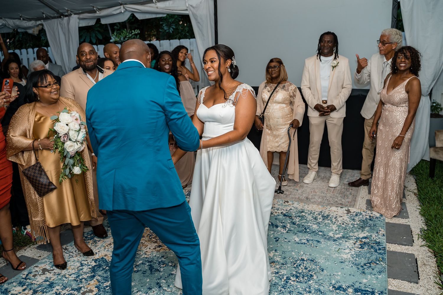 Wedding ceremony with guests watching couple dance on blue patterned carpet under white tent.
