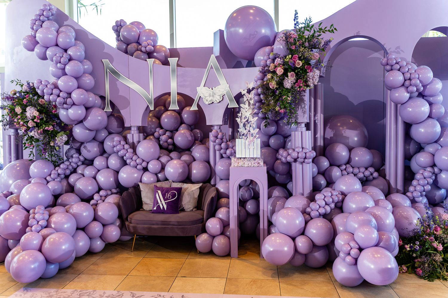 Purple balloon castle themed party setup with floral arrangements and decorative arches.