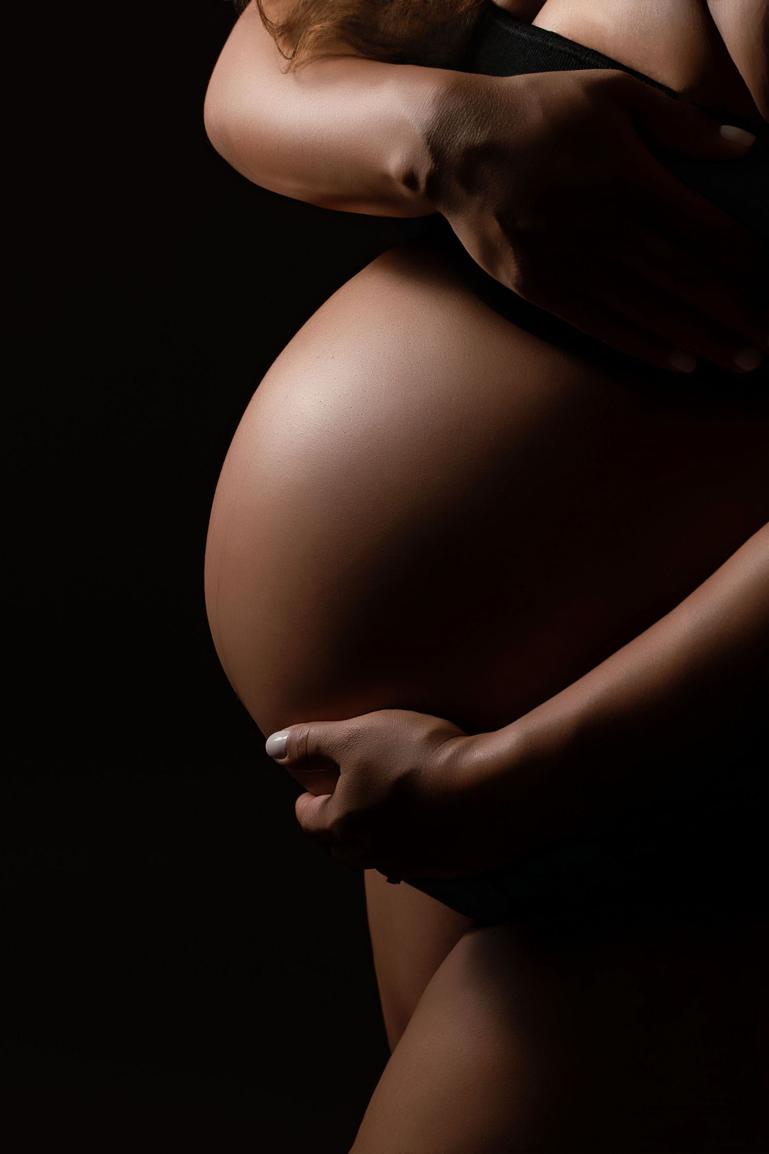 Silhouetted side view of pregnant belly against dark background in artistic maternity photography.
