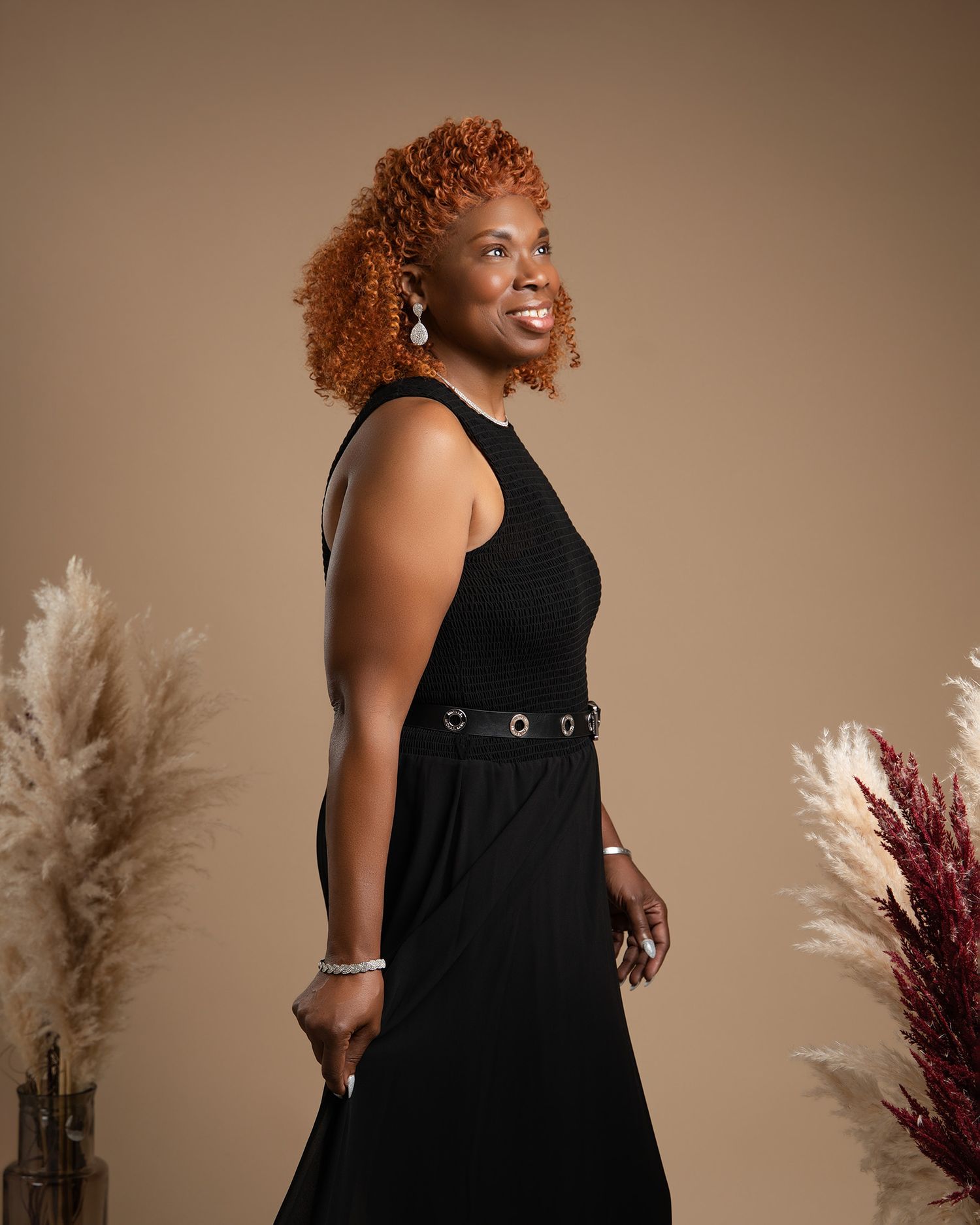 Elegant side profile portrait in black dress with pampas grass decor against neutral backdrop.