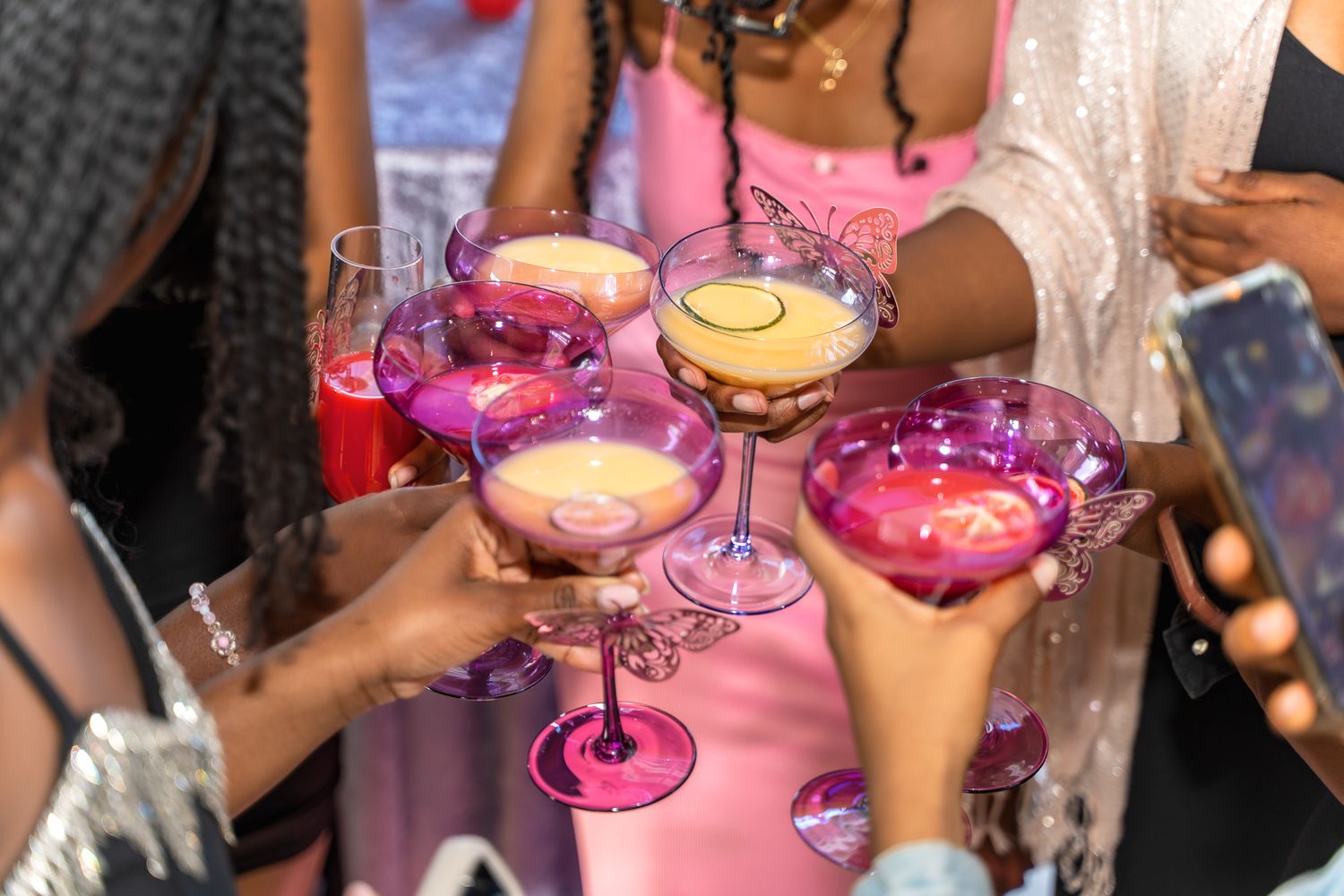 Pink cocktails being toasted during a celebration with multiple glasses raised.