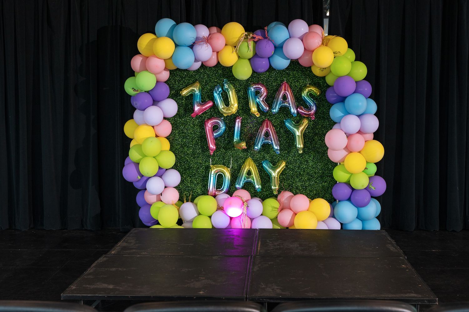 A colorful balloon arch with 'Laura's Play Day' text displayed against a black background.
