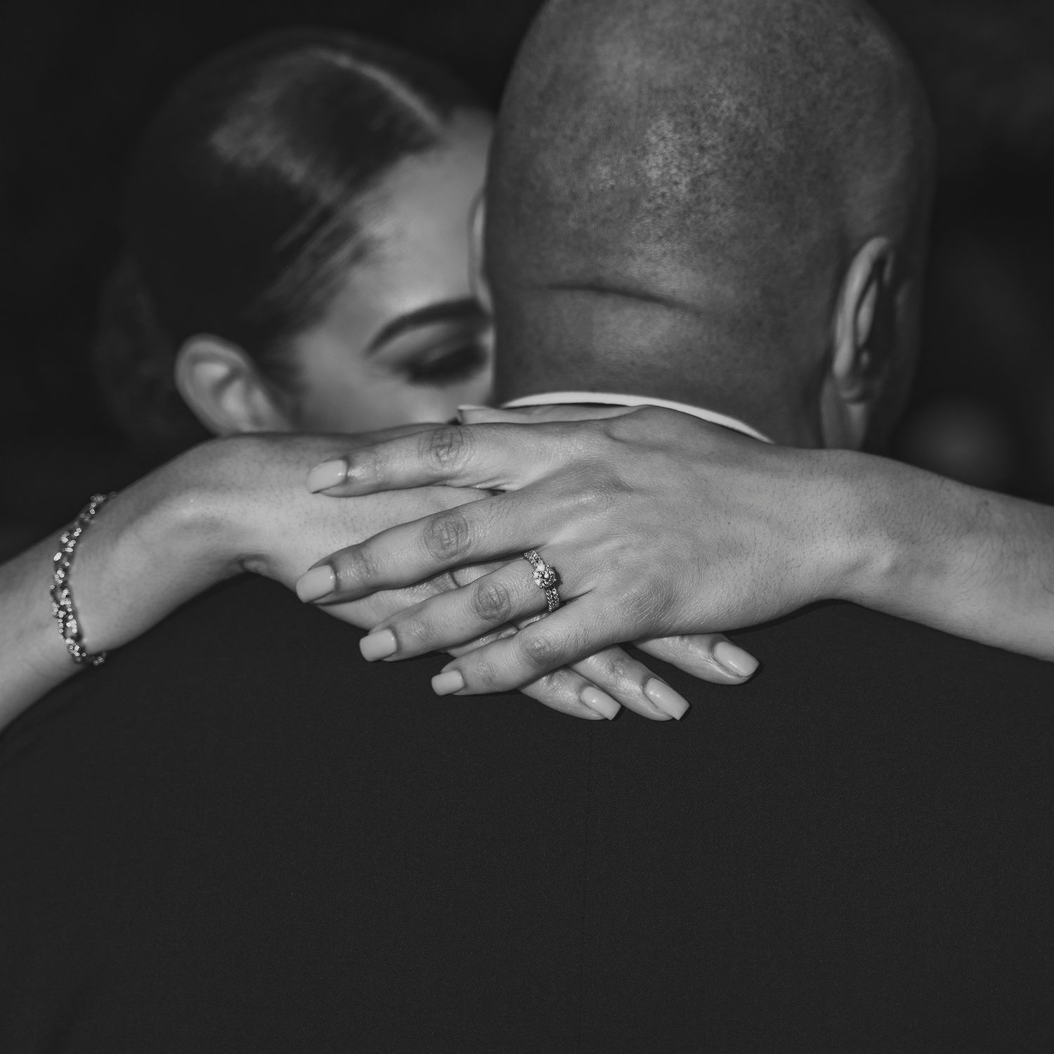 A black and white photograph captures an intimate embrace with hands visible around shoulders.