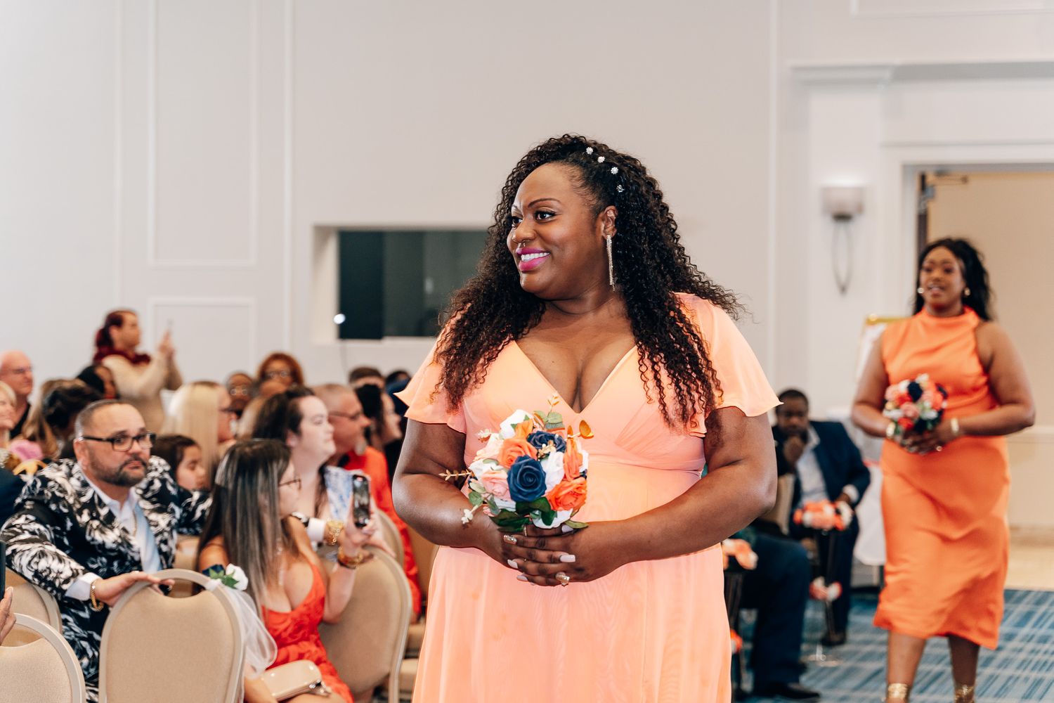 Wedding guests in coral dresses celebrating joyfully at an indoor reception.