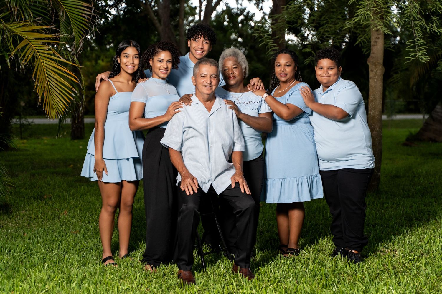 A group in coordinating blue and white outfits poses together on grass during an outdoor photo session.