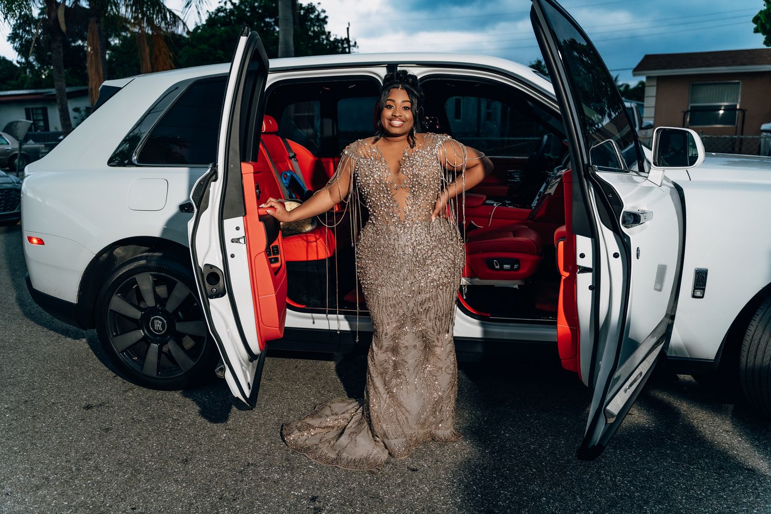 A glamorous beaded evening gown captured next to a luxury white car with red seats.