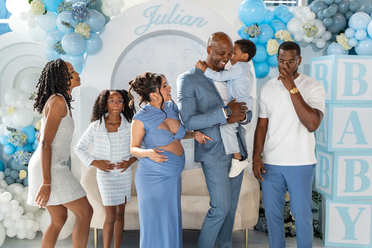 Group photo at a baby shower celebration with blue and white balloon decorations.