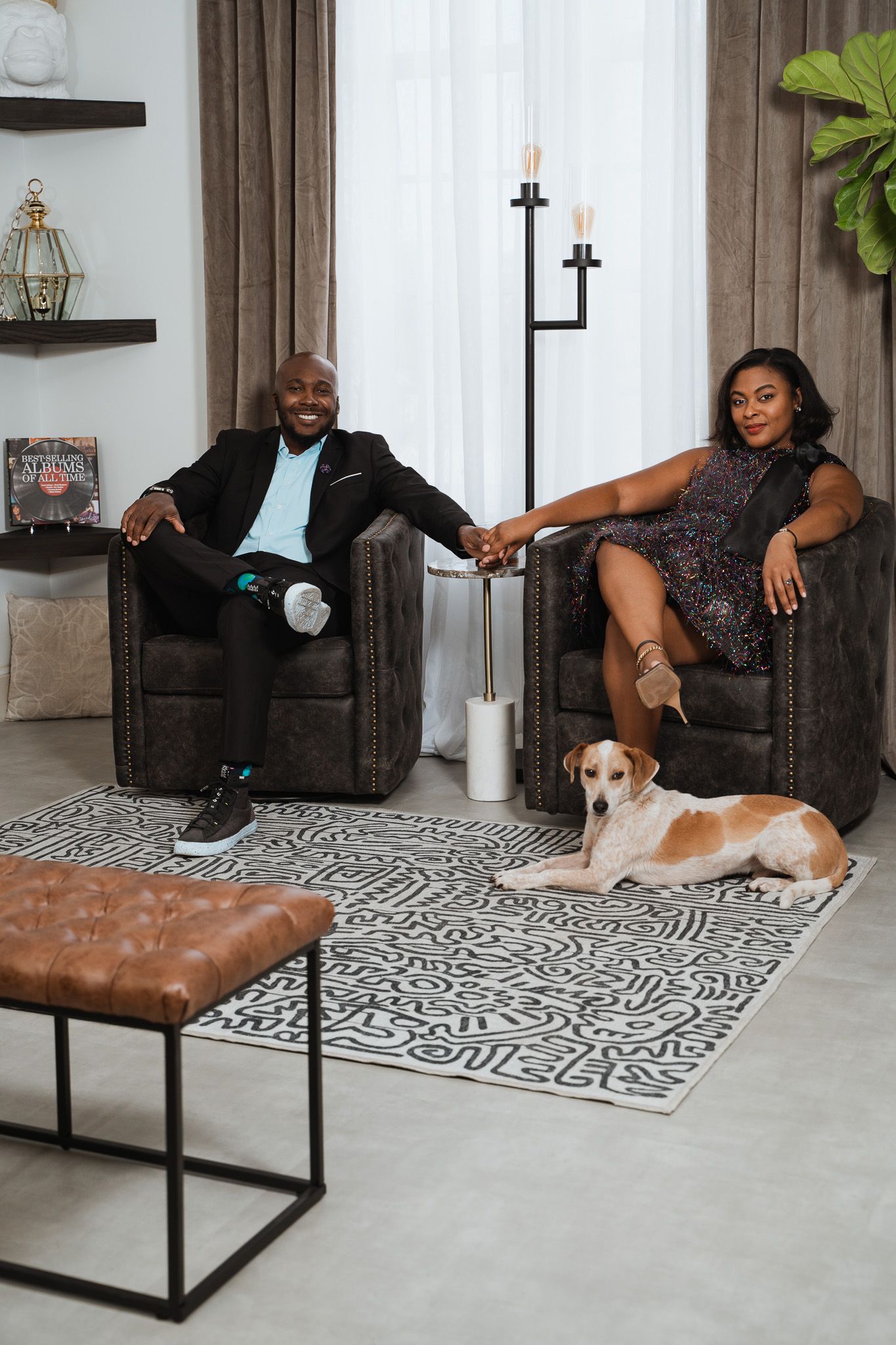 Couple relaxing in leather armchairs with dog on geometric rug in stylish living room.