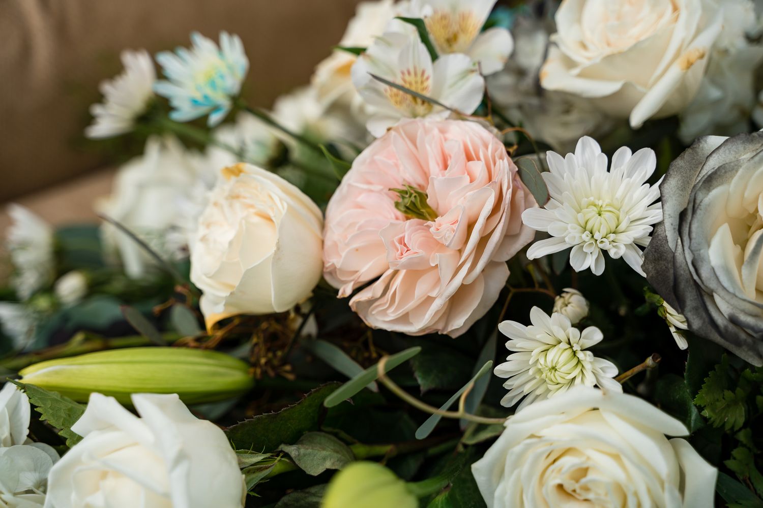 Close-up of delicate pink and white roses with daisies in a wedding floral arrangement.