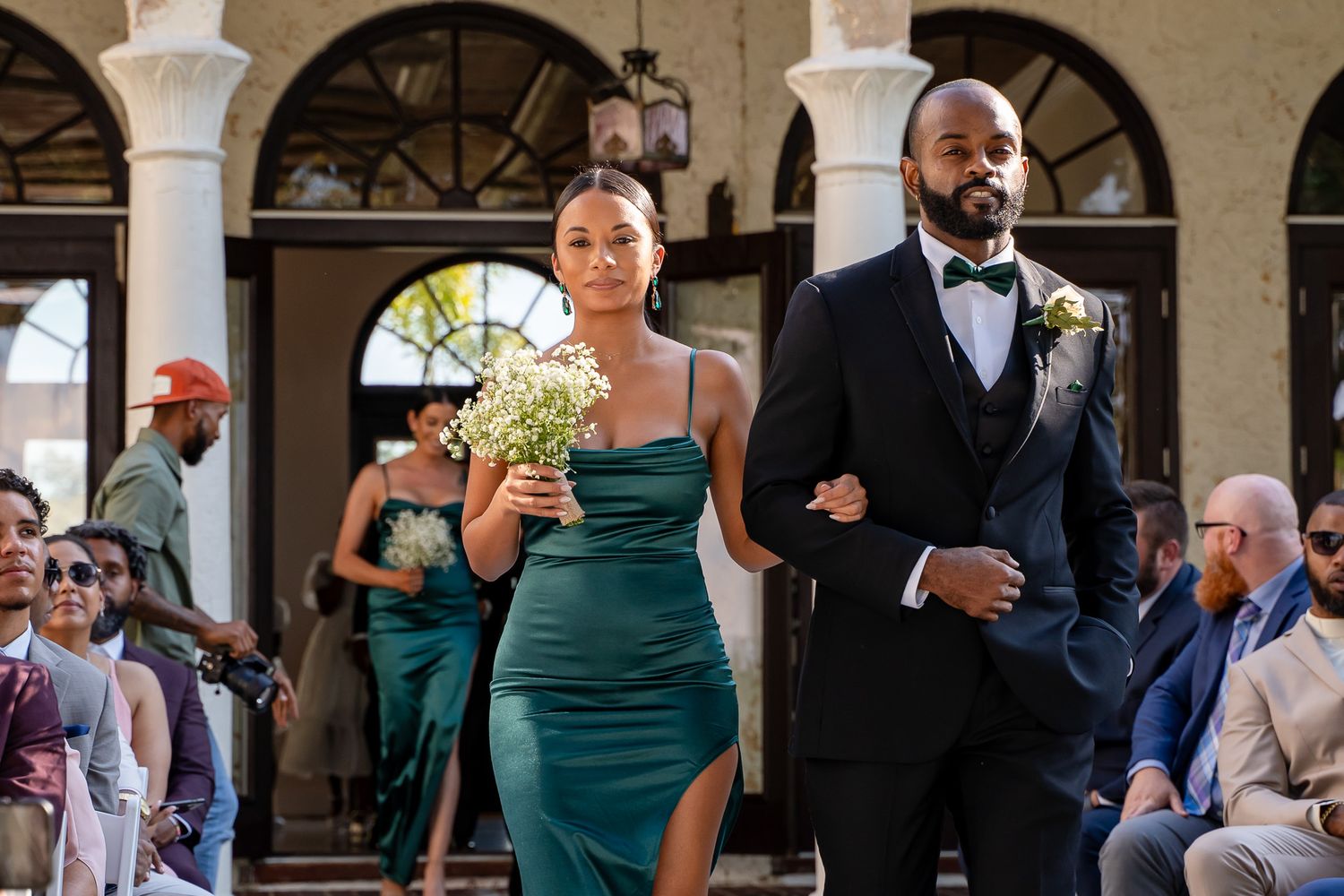 A couple walks arm in arm during a wedding procession through an elegant archway.