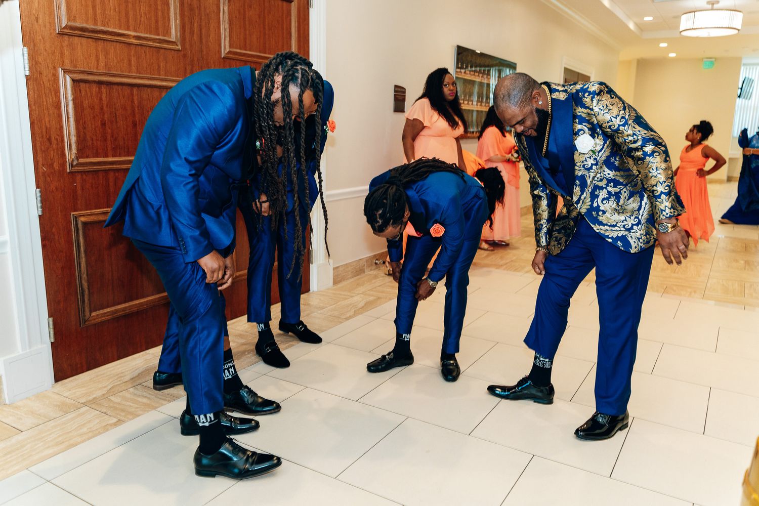Groomsmen in blue suits checking their formal attire before a wedding ceremony.