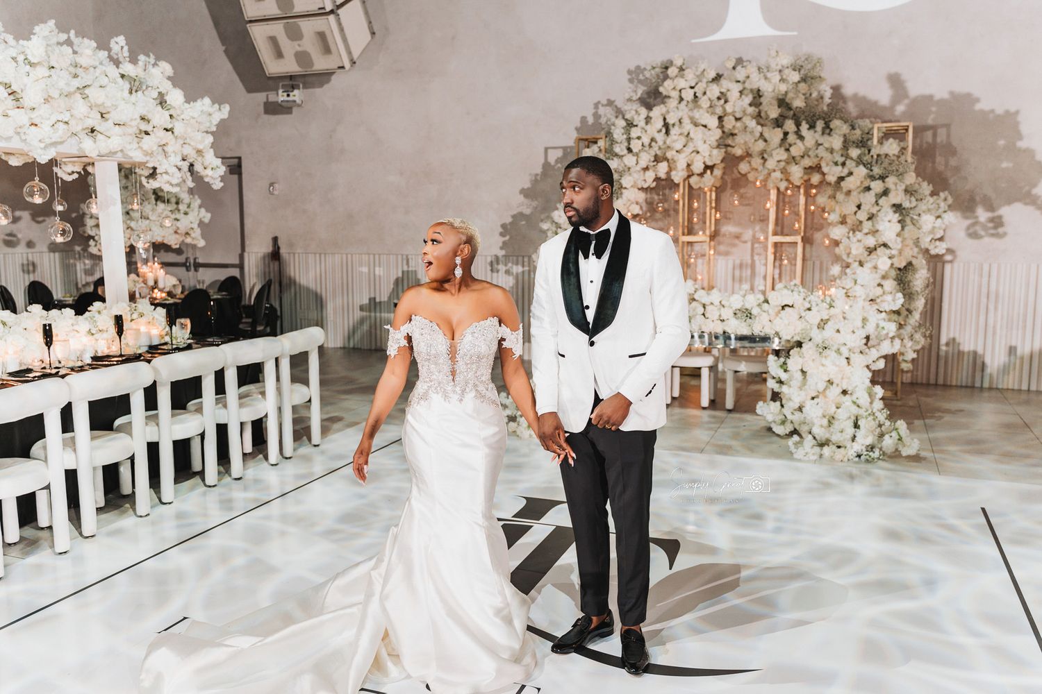 Wedding couple walking together in an elegantly decorated white floral ceremony space.