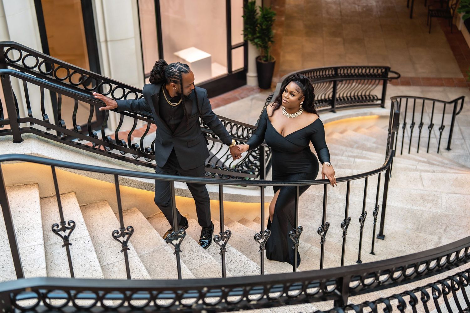A fun couple enjoys a playful moment on an ornate spiral staircase with decorative iron railings.