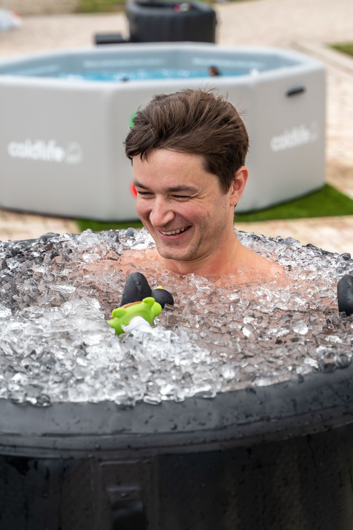 Person enjoying an ice bath with a rubber duck toy in an outdoor spa setting.