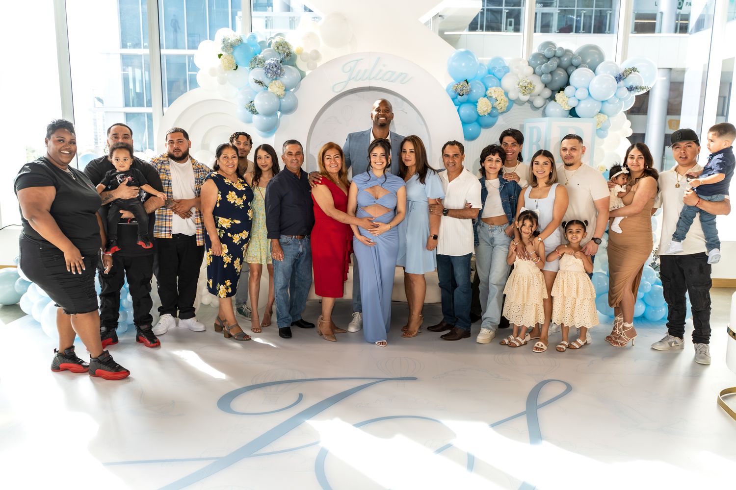 Large group photo of guests gathered at baby shower with blue and white balloon decorations.