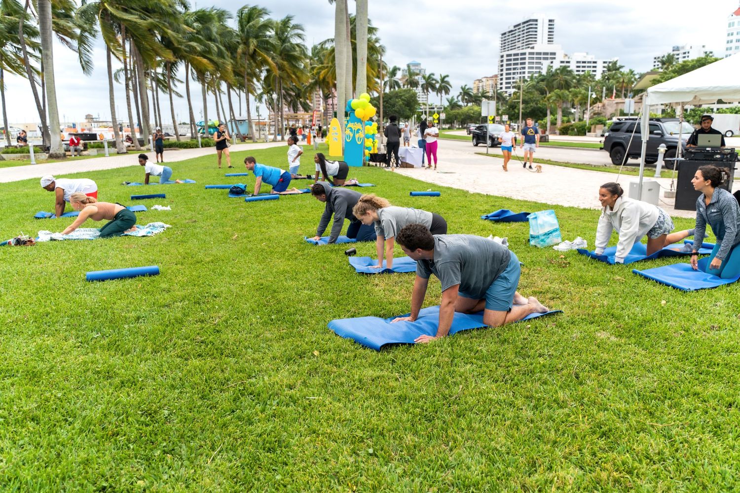 Group fitness class participants exercising on blue yoga mats in a palm tree-lined park by the water.