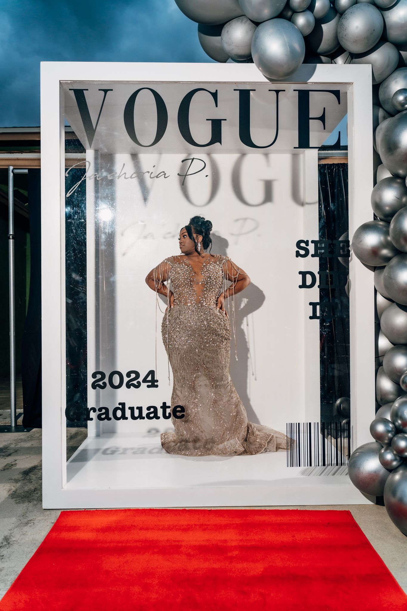 Artistic portrait through oversized Vogue magazine frame with silver balloon arrangement.