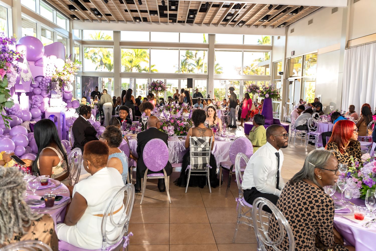 A reception hall decorated in purple with guests seated at round tables for a special occasion.