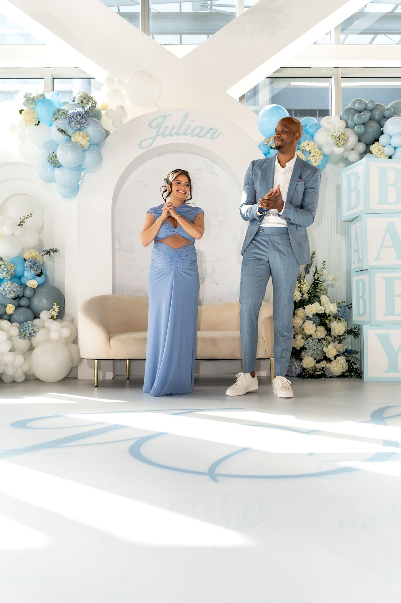 Couple posing in front of blue and white balloon arch at elegant baby shower celebration.