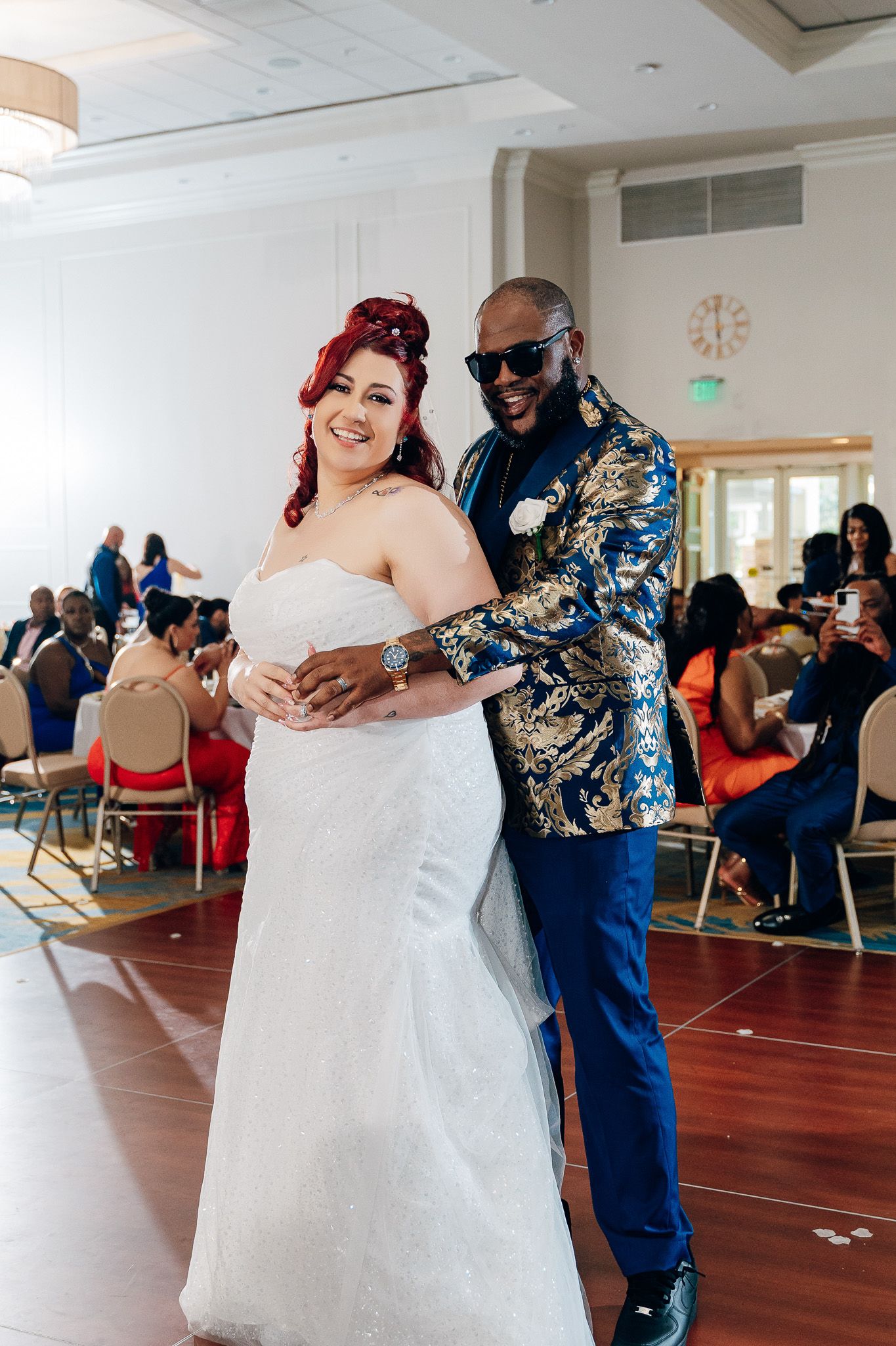 Couple dancing together at wedding reception with guests seated at round tables in background.