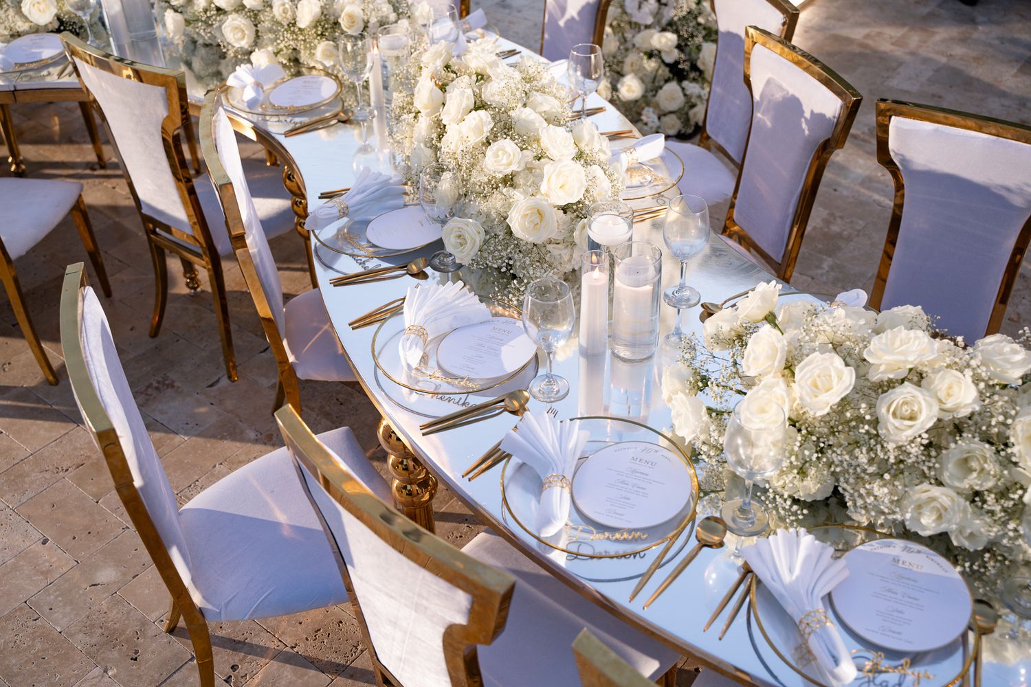 Elegant wedding table setting with white roses and gold accents in a luxurious reception space.