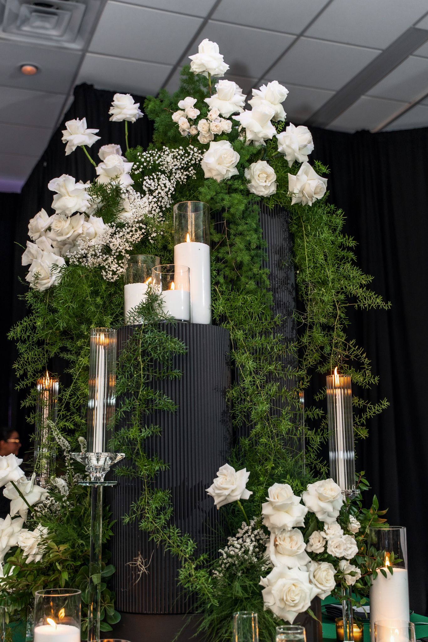 Elegant white rose arrangements with tall glass candle holders and greenery against a black backdrop.